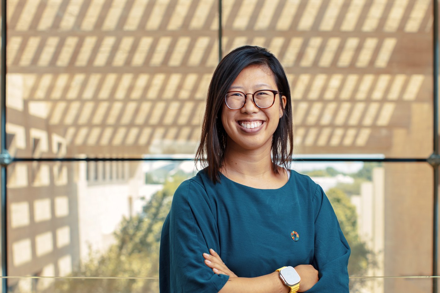 Angela Ng smiling with arms crossed, wearing a teal top and a Sustainable Development Goals pin